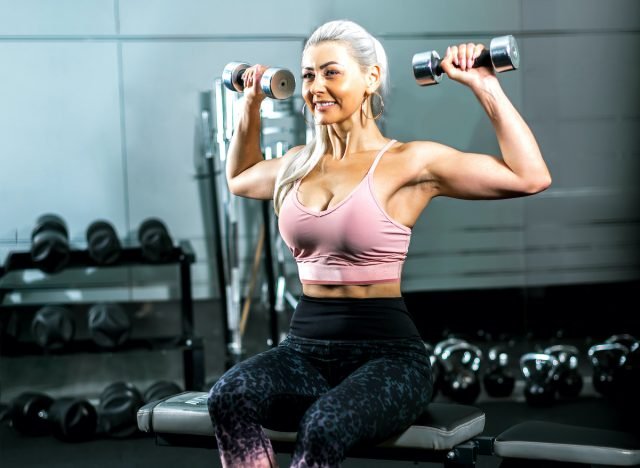 mature, fit and strong woman holding dumbbells flexing muscles in gym, concept of exercises for upper body strength as we age