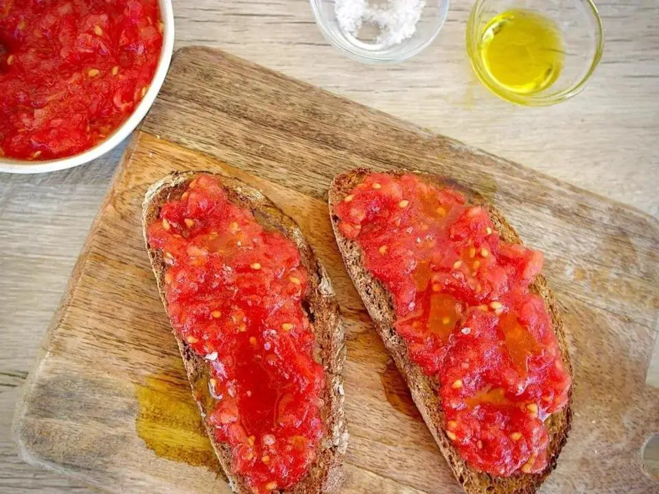 Pan con tomate on a wooden cutting board with bowls of tomato, salt and olive oil