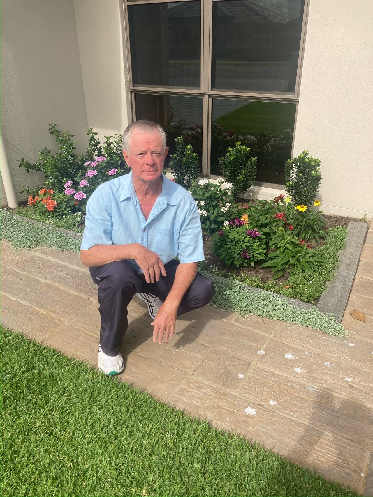 A man wearing a blue shirt and black trousers kneeling outside.