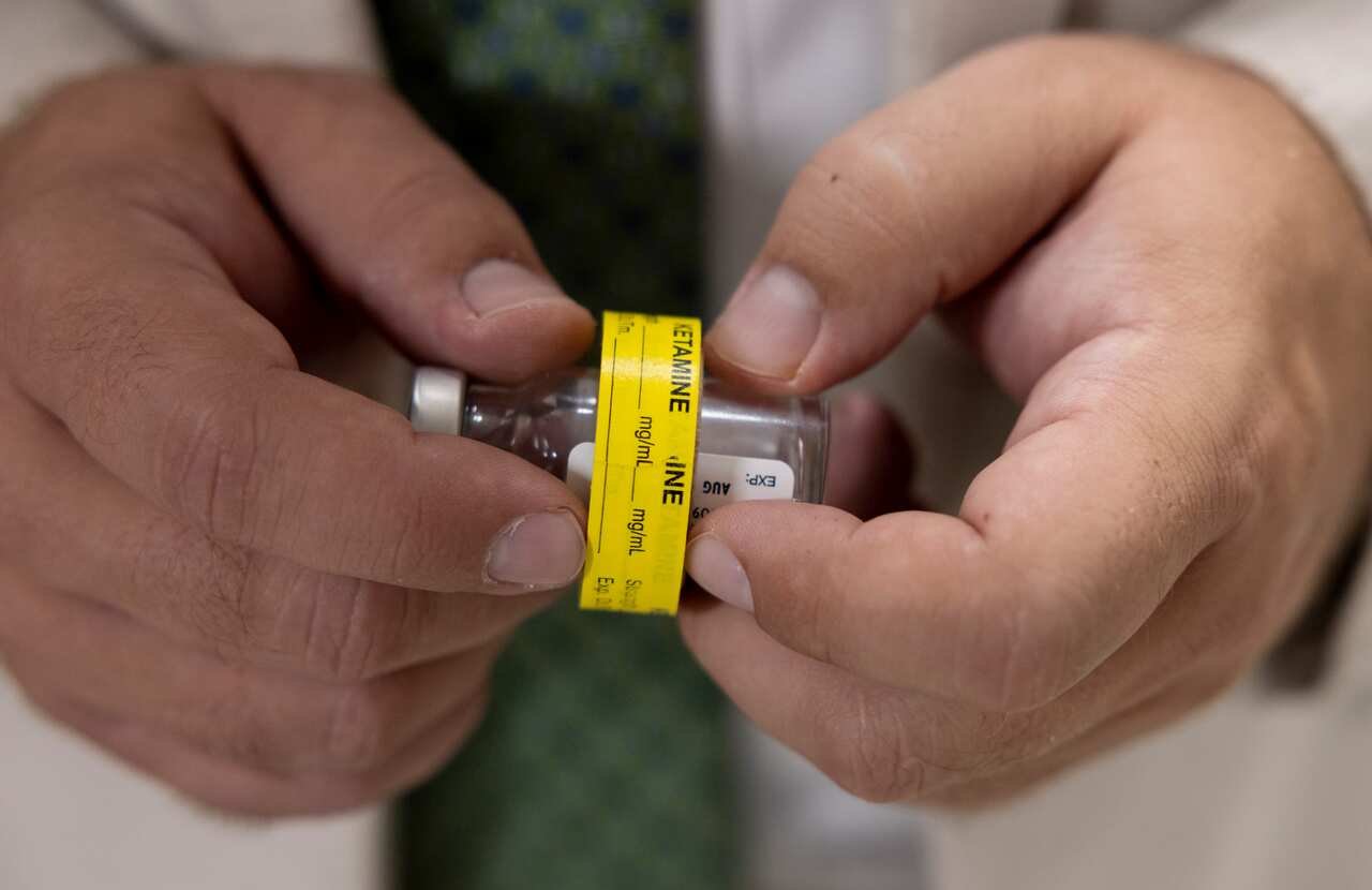 A doctor holding a vial labeled Ketamine.