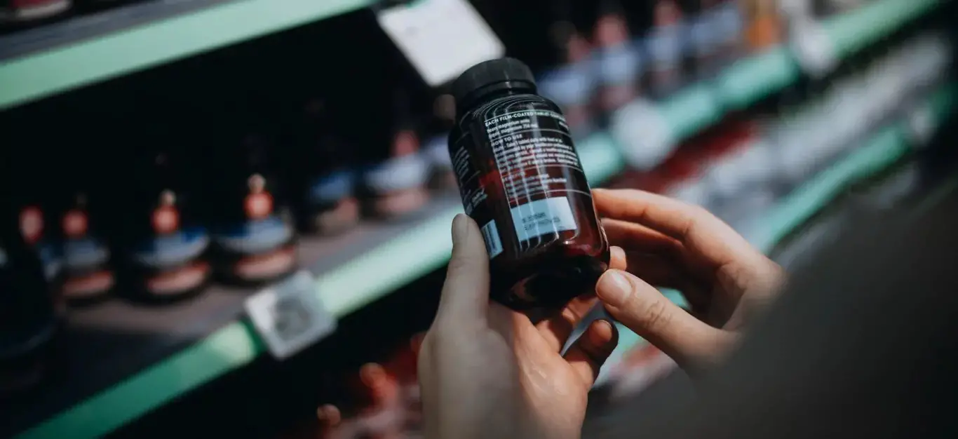 Over the shoulder view of hands holding a bottle of probiotic supplements taken from a grocery store shelf, reading the label