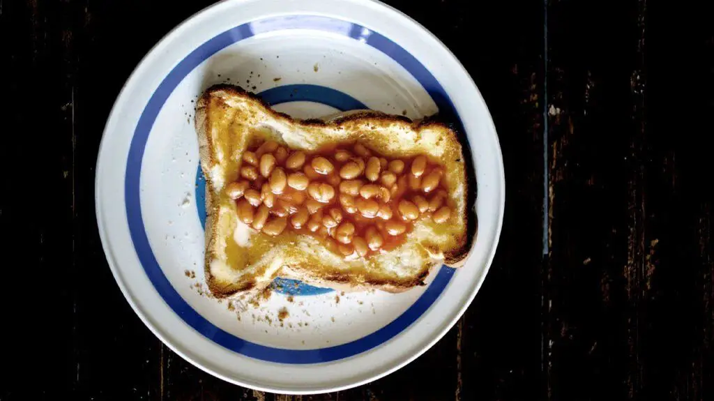 A piece of toast on a plate and baked beans on top