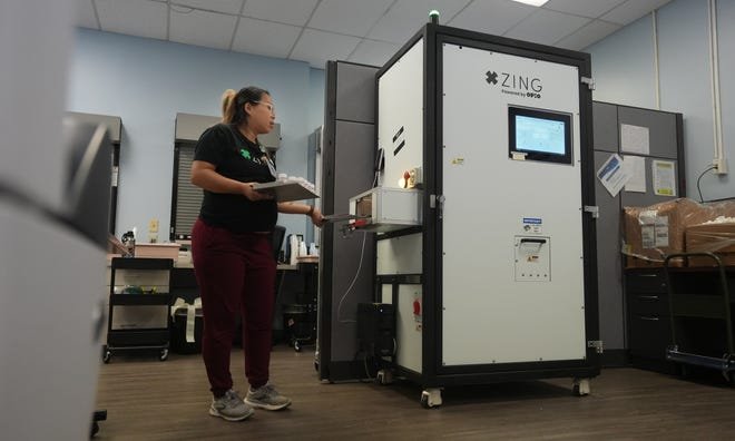 Using a new automated dose assembly machine, Registered Nurse Siv Mao removes a tray of methadone doses that will be dispensed to people with opioid use disorders.  CompDrug made history by being the first opioid treatment program to go live using Zing, which assembles doses automatically.  The innovative machine offers the opportunity to reduce human error, assemble drug doses at a rapid pace, and allow nursing staff to focus on direct patient care.